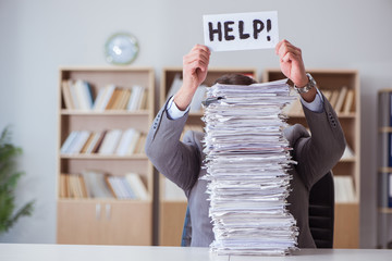 An office worker buried in paperwork, looking stressed and overwhelmed by the towering stacks of documents